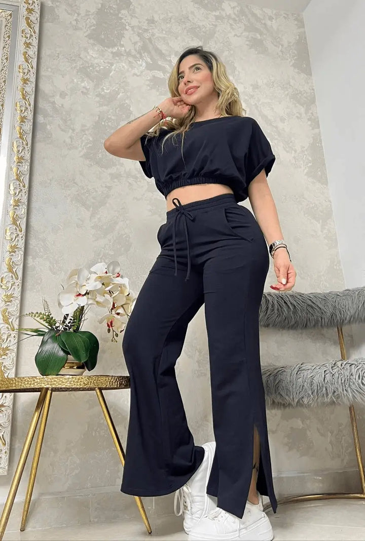 Mujer usando conjunto bota campana negro con top crop de manga corta y pantalón ancho con abertura lateral, combinado con tenis blancos, estilo urbano cómodo y versátil que realza la figura