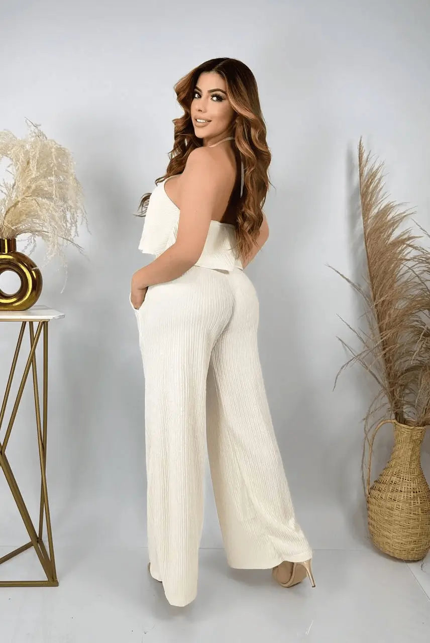Enterizo crema de mujer con tirantes halter y volante en el busto, tejido acanalado suave y ligero, pernera ancha con bolsillos laterales, silueta elegante y cómoda, prenda versátil ideal para looks casuales y eventos formales