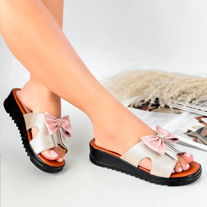 Sandalias de cuero beige con plataforma negra y moño rosa, diseño cómodo y elegante para mujer, ideal para uso diario y piel delicada, suela antideslizante que brinda estabilidad y confort en cada paso.