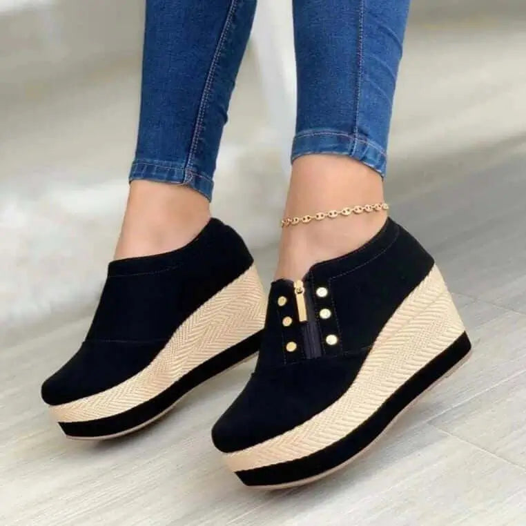 Tacones negros con plataforma alta en cuña de yute, cierre lateral dorado y detalles decorativos, ideales para dar altura y estilo cómodo en cualquier ocasión casual o formal, combinan con jeans y atuendos modernos, diseño ergonómico que aporta soporte y estabilidad al caminar.