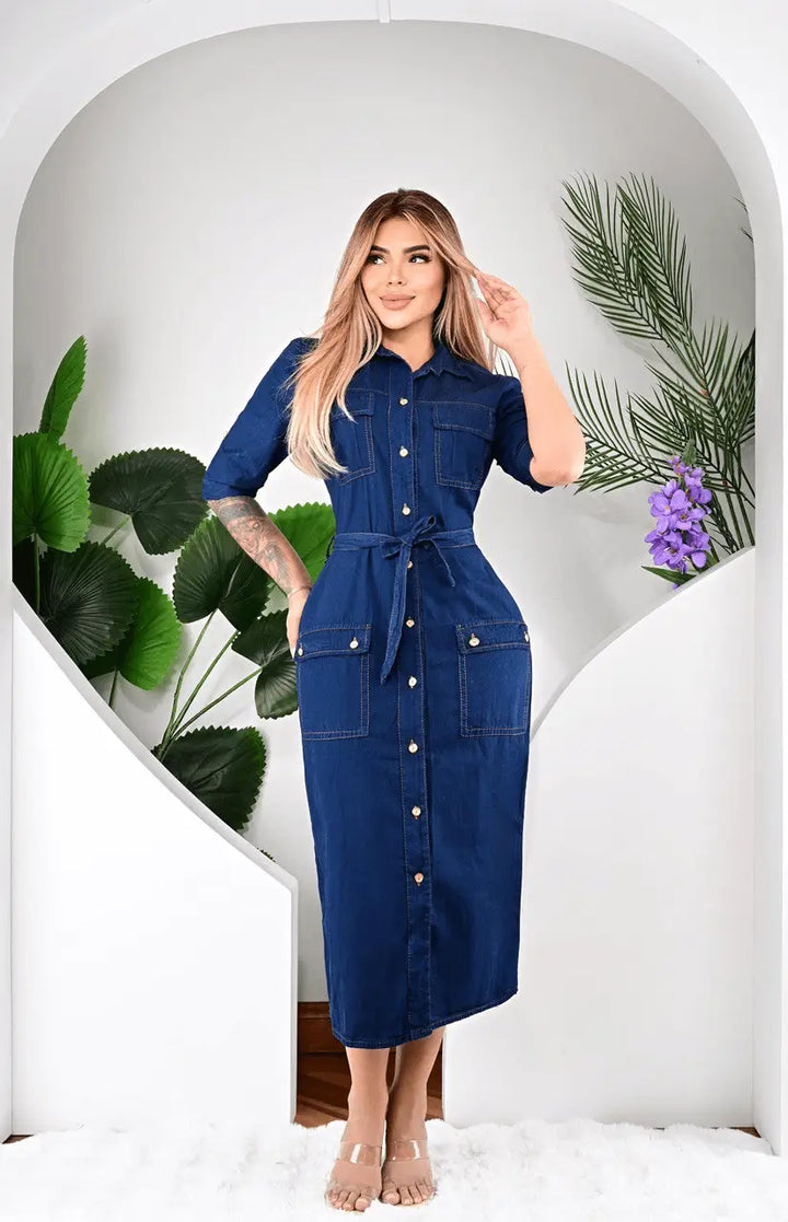 Mujer luce vestido largo de jean azul oscuro estilo denim con botones dorados, cinturón ajustable, bolsillos frontales, corte midi cómodo y versátil para uso casual y urbano