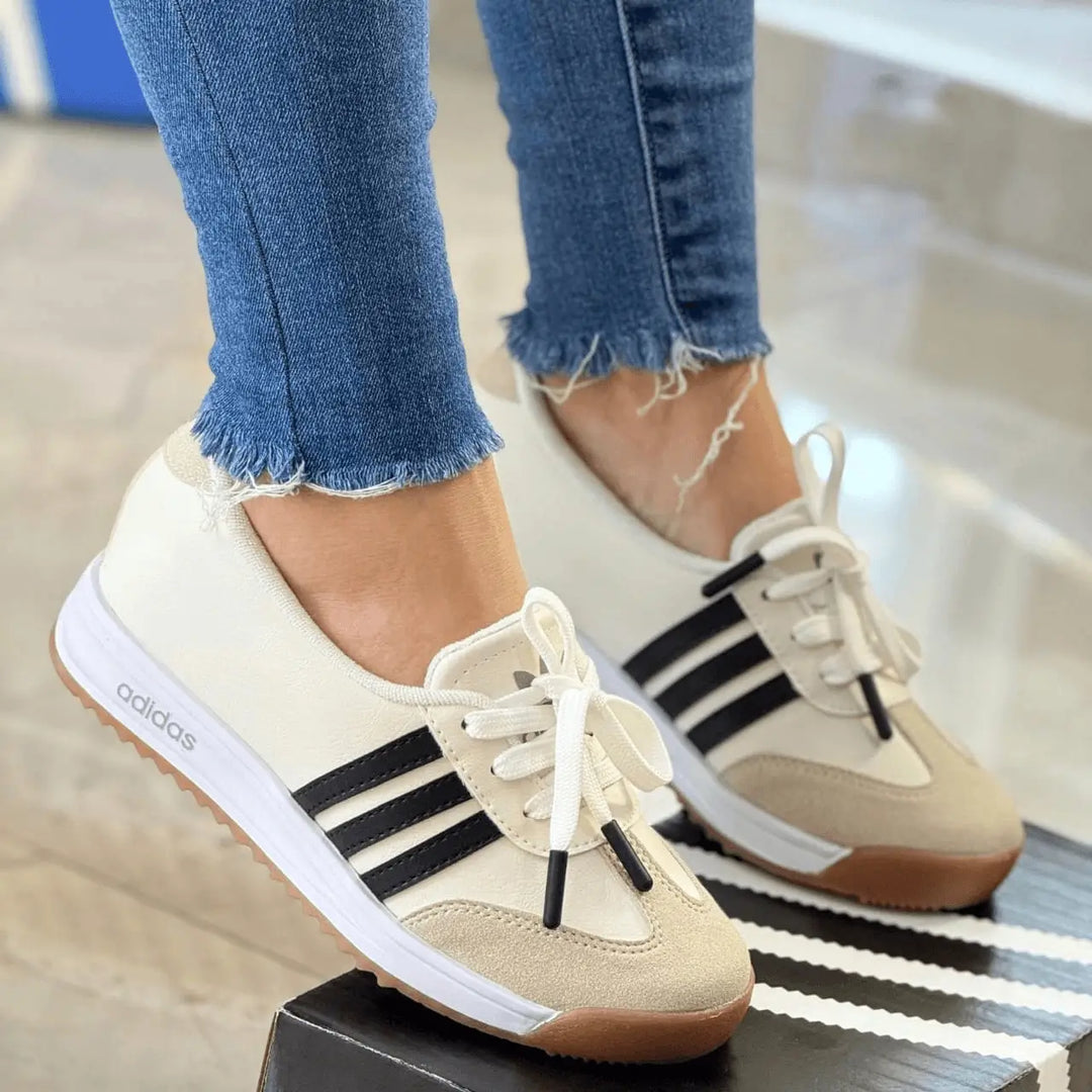 Zapatillas deportivas estilo retro color crema con franjas negras, suela de goma antiderrapante y plantilla acolchada que ofrece confort y soporte en cada paso, diseño ligero y versátil ideal para uso diario y look casual en ciudad