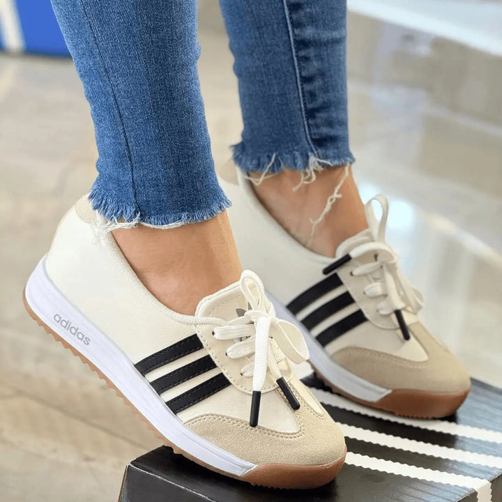 Zapatillas deportivas estilo retro color crema con franjas negras, suela de goma antiderrapante y plantilla acolchada que ofrece confort y soporte en cada paso, diseño ligero y versátil ideal para uso diario y look casual en ciudad