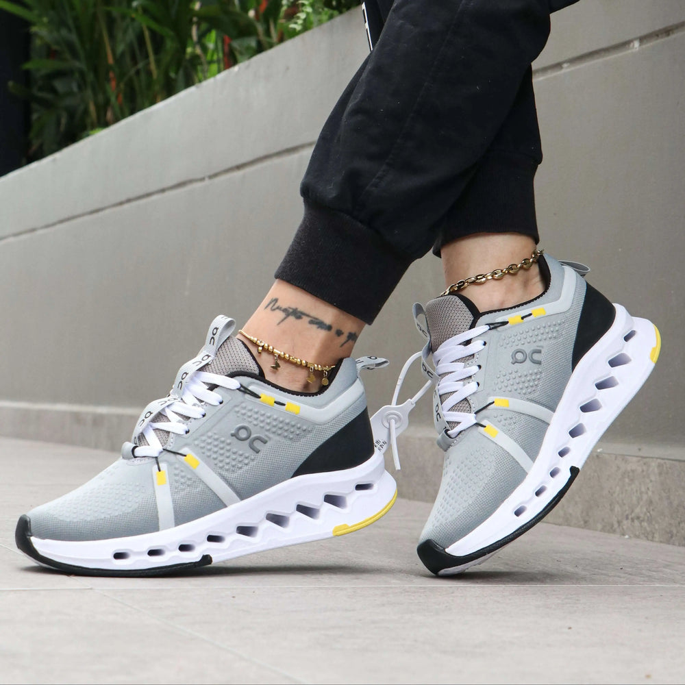 Zapatillas deportivas grises con detalles en amarillo, diseño moderno y transpirable, suela acolchonada para máxima amortiguación y confort al caminar o entrenar, ideales para correr y uso diario en ciudad.