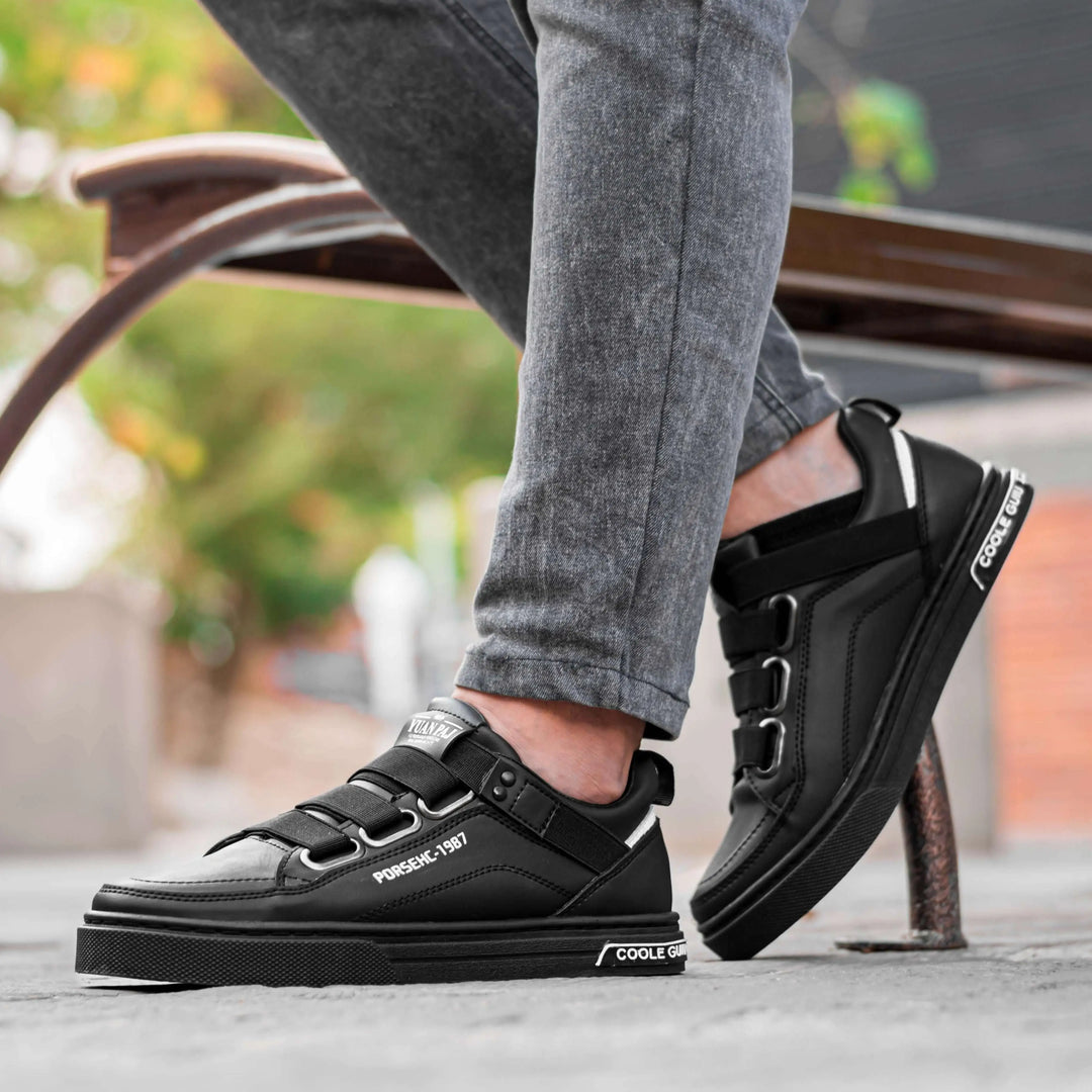 Zapatos deportivos negros para hombre con diseño moderno y detalles en blanco, fabricación en material sintético resistente y cómodo, suela antideslizante para mayor seguridad, ideales para uso urbano y casual, estilo versátil que combina con jeans y pantalones ajustados.
