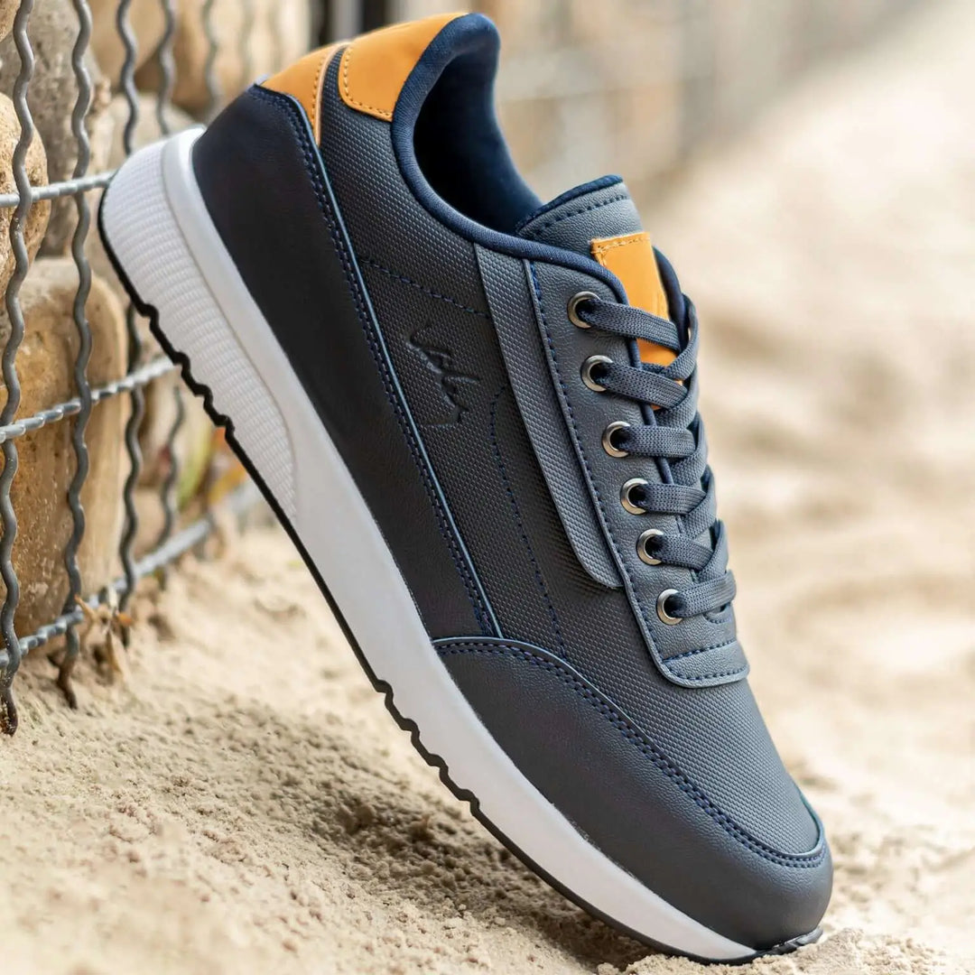 Zapatilla deportiva para hombre en tonos azul marino y mostaza, confeccionada con materiales transpirables y durables, suela antideslizante blanca ideal para uso diario y actividades casuales, diseño moderno y cómodo que brinda soporte y estilo para caminar todo el día.