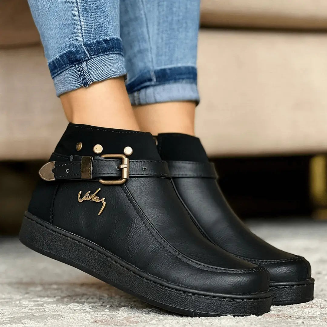 Botín negro para mujer en material sintético de alta calidad, con diseño elegante y cómodo, suela antideslizante ideal para uso diario, cierre lateral y detalle de hebilla decorativa que aporta estilo sofisticado, perfecto para combinar con jeans o pantalones casuales.