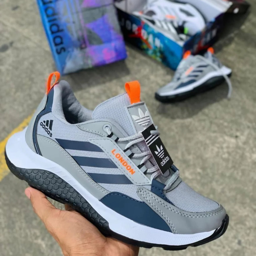 Zapatillas London en gris con detalles naranja, tiradores en el talón y la lengüeta y entresuela blanca amortiguada.