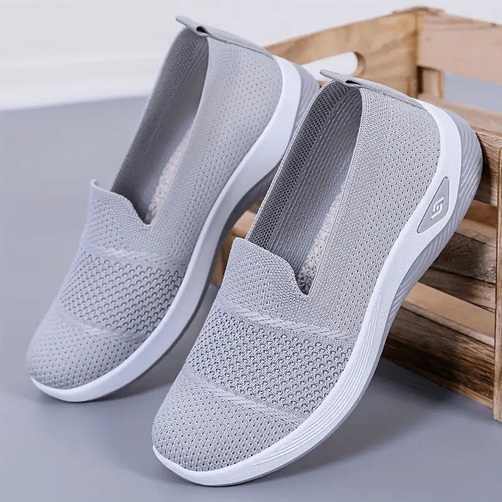 Zapatillas livianas para mujer en color gris claro, diseño transpirable de malla, suela blanca antideslizante y flexible, calzado cómodo ideal para uso diario y caminatas, fácil de poner y quitar, perfectas para quienes buscan comodidad y estilo casual.