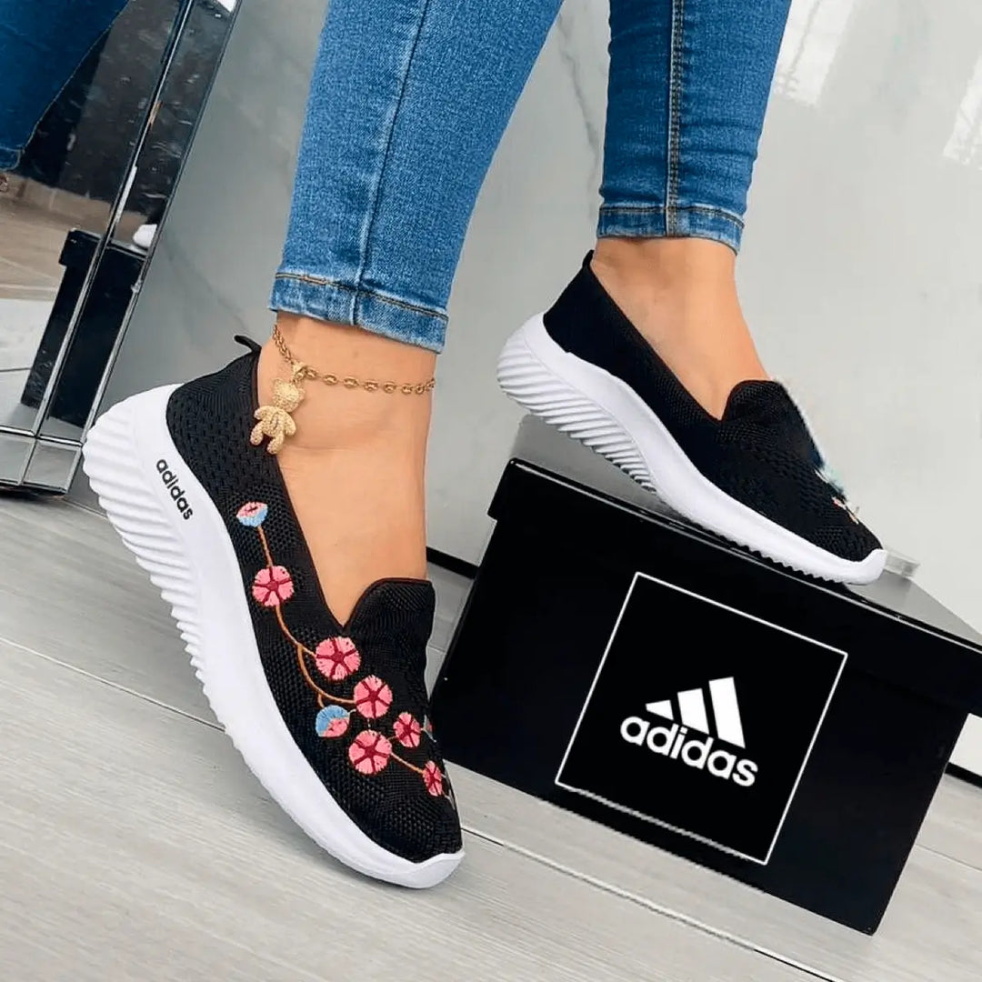 Zapatillas deportivas negras con diseño floral bordado en colores rosa y azul, suela blanca antiderrapante, cómodas y livianas ideales para uso diario y caminar largas distancias, combinación perfecta de estilo y funcionalidad para mujeres jóvenes y activas.