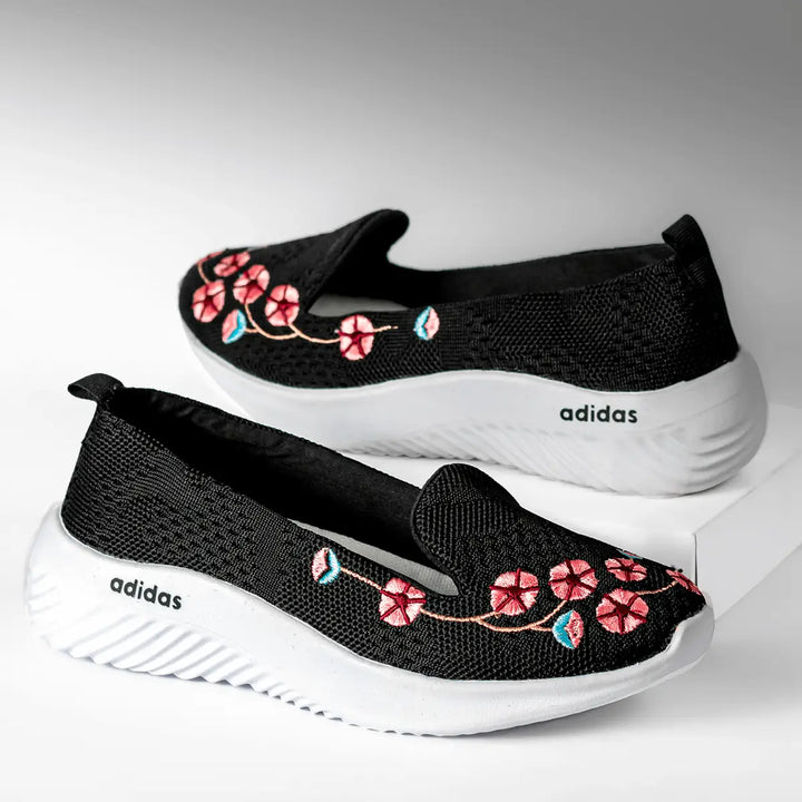 Zapatillas negras con diseño floral bordado en tonos rosas y azules, suela blanca antiderrapante ligera y cómoda, ideales para uso diario, con tejido transpirable que proporciona frescura y estilo moderno casual para mujeres que buscan confort y elegancia.