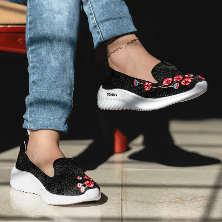 Zapatillas negras con diseño floral bordado en rojo y azul, suela blanca antideslizante, cómodas y ligeras, ideales para uso diario y estilo casual, perfectas para mujeres jóvenes que buscan moda y confort acordes a las últimas tendencias en calzado.
