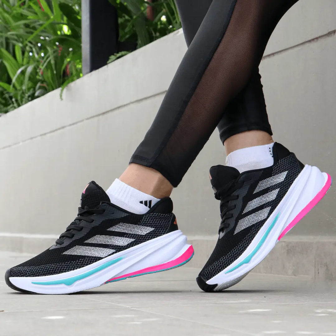 Zapatillas deportivas negras con detalles en blanco, suela blanca con acentos rosas y azules, diseño liviano y transpirable ideal para running, entrenamiento y uso casual, con máxima amortiguación y soporte para confort durante todo el día.