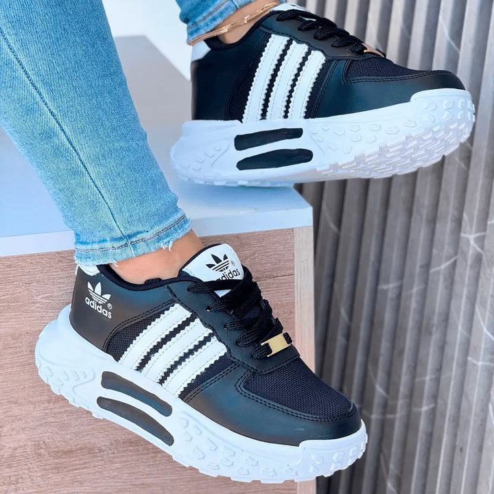 Zapatillas deportivas negras con detalles blancos y suela gruesa tipo tractor, diseño moderno y cómodo. Ideales para uso diario y actividades al aire libre, ofrecen buena amortiguación, soporte en el pie y estilo casual para combinar con jeans. Calzado resistente, transpirable y con agarre antideslizante, perfectas para caminar largas distancias con comodidad y duración.