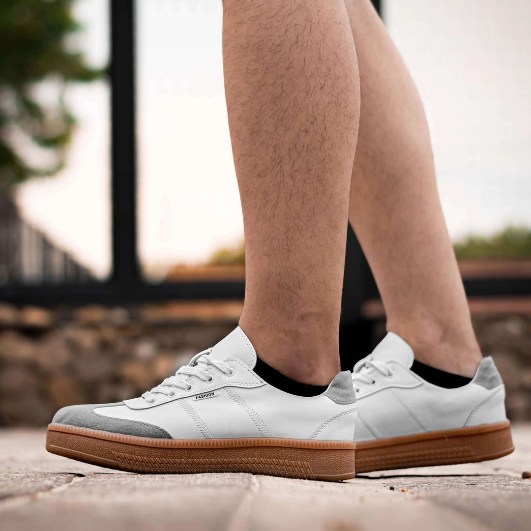 Zapatos blancos para hombre estilo casual con suela de goma color café, diseño cómodo y resistente, ideales para uso diario, con cierre de cordones y detalles grises en punta y talón que ofrecen durabilidad y soporte al pie.
